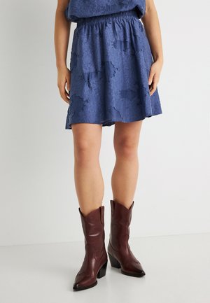 Μπλε υφασμάτινη φούστα με ελαστική μέση, σε συνδυασμό με καφέ δερμάτινα καουμπόικα μποτάκια με μυτερά δάχτυλα και τετράγωνες φτέρνες.