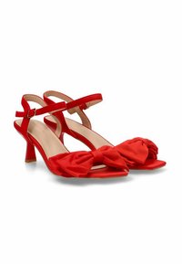 Sandalias de tacón rojo con textura suave, diseño de puntera abierta, detalle de lazo en la parte frontal y correa ajustable en el tobillo con hebilla.