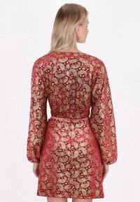 Rotes Kleid mit goldenen Paisley-Muster, langen Ärmeln, tailliertem Schnitt und kurzem Rock. Verfügt über ein Rückendetail mit einem Reißverschluss.