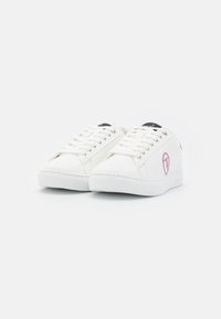 White sneakers with a smooth leather upper, round toe, contrasting pink logo on the side, and flat laces. Textured rubber sole for grip.