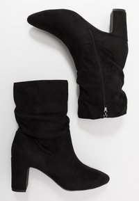 Černé semišové kotníkové boty s špičatou špičkou a blokovým podpatkem. Mají volnější horní část a zip na vnější straně pro snadnější oblékání.