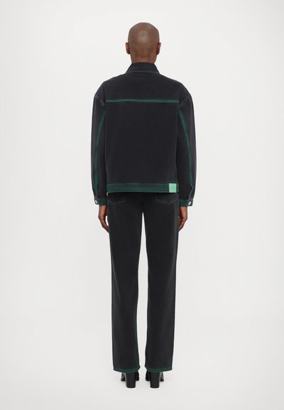 Veste en denim noir et pantalon avec des coutures et des accents verts. La veste présente un col et une fermeture à boutons, tandis que le pantalon est large avec des détails sur l'ourlet.