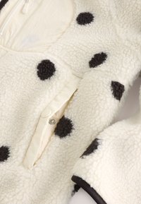 Close-up of cream-colored sherpa jacket with black polka dots, showing snap button closure and textured fabric.