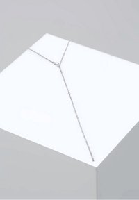 Collier délicat en chaîne argentée avec un design en forme de Y, présenté sur un cube blanc sur un fond gris clair.