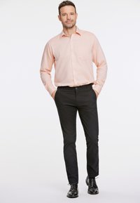 Camisa de manga larga rosa claro con un bolsillo en el pecho, combinada con pantalones ajustados negros y zapatos de cordones negros. Textura suave, ajuste a medida.