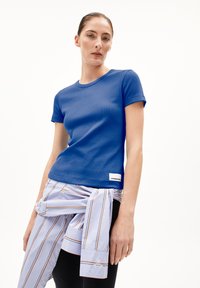 Blauw ribbed t-shirt met korte mouwen en een aansluitende snit, met een label aan de onderkant. Gecombineerd met een lichtblauw gestreept shirt dat om de taille is geknoopt.