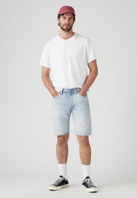 Shorts din denim albastru deschis, tricou alb cu guler rotund, șapcă roșie, adidași negri cu talpă albă și șosete albe; design casual, simplu.