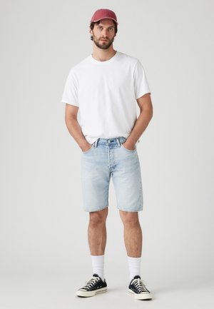 Shorts en denim bleu clair, t-shirt blanc à col rond, casquette rouge, baskets noires avec semelles blanches et chaussettes blanches ; design décontracté et simple.