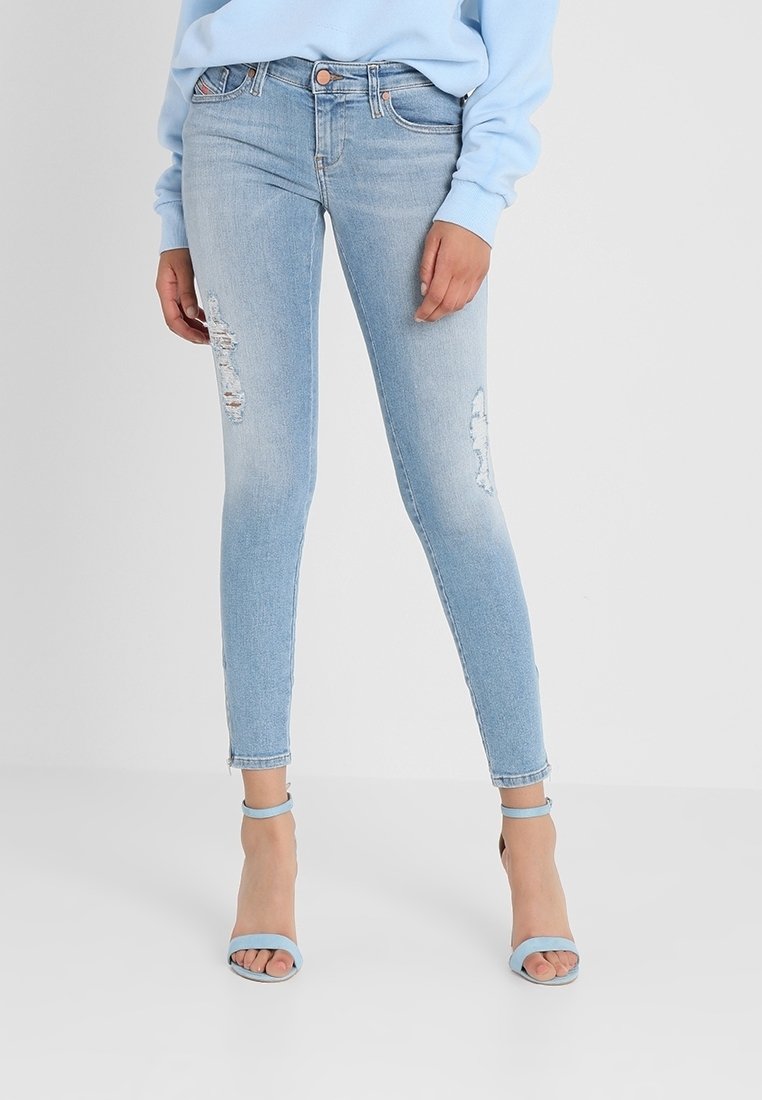 Vaqueros ajustados de color azul claro con parches desgastados, hechos de mezclilla. Presentan una cintura de altura media y corte hasta el tobillo. Combinados con sandalias de tacón azules.