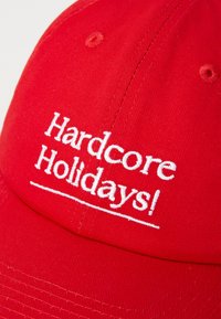 Bască roșie de baseball cu text brodat alb care citește "Sărbători Hardcore!" Prezintă un design structurat și un material texturat.