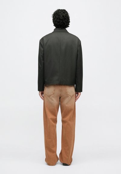 Čierna bunda z umelého kože s rovnakým strihom a výrezom s výstrihom, v kombinácii so svetlohnedými, zúženými džínovými nohavicami s vyblednutým efektom.