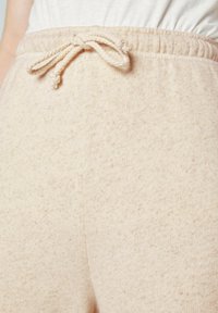 Beige, gestructureerde sweatpants met een elastische tailleband en een trekkoord. De stof heeft een subtiele gemêleerde patronen.