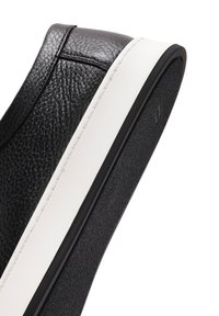 Scarpa slip-on in pelle nera con superficie testurizzata, suola intermedia bianca e suola esterna in gomma nera. Cuciture visibili lungo il bordo.