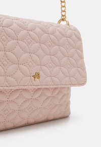 Bolso de mano de cuero acolchado rosa con una correa de cadena. Presenta patrones circulares en relieve y un pequeño logotipo dorado en la parte delantera.