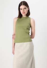 Ribbade gröna ärmlösa toppen med hög halsringning, kombinerad med en ljusbeige kjol. Det släta tyget och den figurnära designen betonar siluetten.