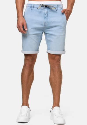 Shorts en denim bleu clair avec des ourlets retroussés, poches avant et un cordon de serrage à motif. Portés avec des baskets blanches, affichant un look décontracté.