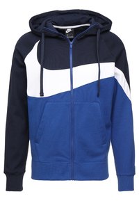 Modrá a námořnicky modrá mikina s kapucí na zip s bílými akcenty, vybavená klokankovou kapsou a kapucí s nastavitelným stahováním. Měkká tkanina.