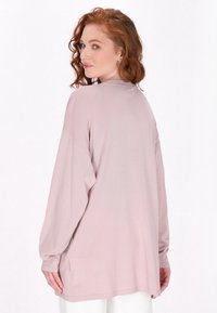 Top a maniche lunghe, di colore rosa chiaro, con una vestibilità morbida. Presenta un colletto rotondo e una texture sottile, realizzato in tessuto morbido con spacchi laterali.