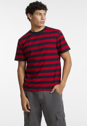 T-shirt rayé rouge et marine en tissu coton, avec un col rond et un logo brodé sur la poitrine. Manches courtes, coupe décontractée.