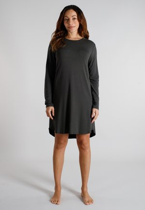 Woman standing barefoot wearing a long-sleeve, knee-length dark gray dress with a round neckline, against a plain light background.