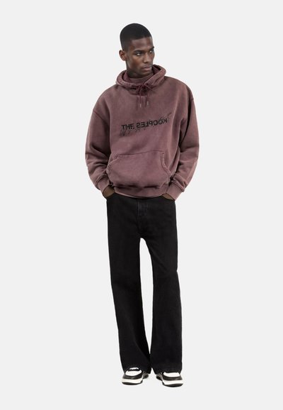 Bordeaux hoodie met een voortas en zwarte tekst. Gepaard met zwarte corduroy flared broeken en zwart-witte sneakers.