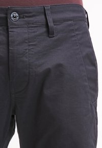 Mörkgrå byxor gjorda av slät tyg, med knappstängning, bältesöljer och rak passform med sidofickor.