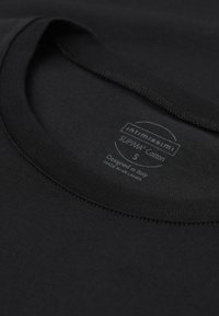 Gros plan sur l'encolure d'un T-shirt en coton noir avec une étiquette imprimée indiquant la taille small et l'origine du design Italie, fabriqué au Sri Lanka.