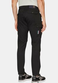 Zwarte cargobroek met meerdere zakken, knoopsluitingen en geborduurde patches. Draag met zwart en grijs sportschoenen.