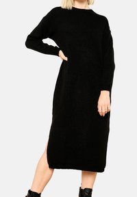 Svart stickad klänning med långa ärmar, avslappnad passform, sidoklyftor, ribbad nederkant och en mjuk textur, som når till mitten av vadder.
