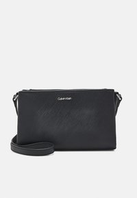 Borsa a tracolla nera Calvin Klein, realizzata in materiale testurizzato, con chiusura a zip e tracolla regolabile con logo in rilievo.