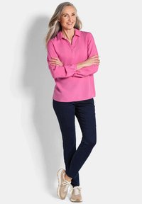 Rosa Bluse mit Kragen und langen Ärmeln, kombiniert mit navyblauen Hosen und beigen Sneakers. Glatte Textur, lockere Passform. Einfaches Design in einfarbig.