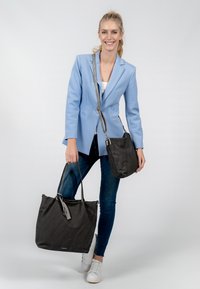 Borsa tote nera in tessuto con due manici, un accento a nappina e una borsa a tracolla più piccola, anch'essa nera, su uno sfondo chiaro.