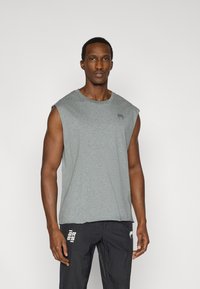 Γκρι αθλητική αμάνικη μπλούζα με στρογγυλή λαιμόκοψη και διακριτικό λογότυπο. Συνδυασμένη με μαύρο ελαφρύ παντελόνι που έχει λευκές λεπτομέρειες.