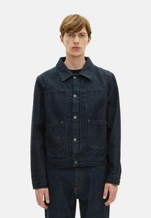 Veste en denim foncé avec un col, boutons sur le devant, deux poches poitrine et des détails de couture visibles. Texture décontractée, coupe ample.