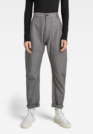 Grå bukser med høj talje, forlommer og en afslappet pasform. Stoffet er glat med en let glans, stylet med opfoldede afslutninger og hvide sneakers.