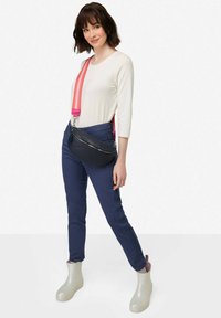 Černá klenutá crossbody taška se stříbrným zipem, v kombinaci s námořnickými kalhotami s bočními pruhy a světlejšími lesklými kotníkovými botami.