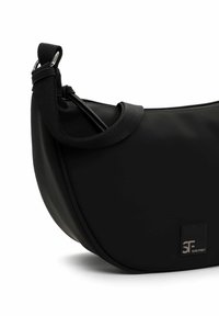 Czarna torebka typu hobo o gładkiej teksturze, zaokrąglonym kształcie i szerokim, regulowanym pasku. Posiada srebrną naszywkę z logo i minimalistyczny design.