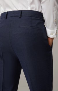 Marineblå skræddersyede bukser i et tekstureret stof, slim fit, to baglommer og en glat talje. Sammen med en hvid skjorte.