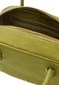 Grøn stof taske med en glat tekstur, der har en guldfarvet lynlås og en indvendig lynlåslomme. Håndtag lavet af matchende grønt materiale.