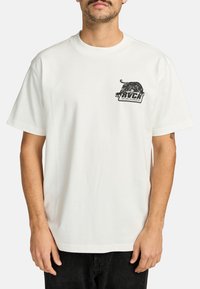 Witte katoenen T-shirt met korte mouwen. Heeft een zwart grafisch ontwerp van een tijger en tekst op de linkerkant van de borst. Eenvoudig ontwerp met ronde hals.