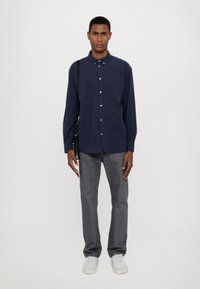 Marine gestreepte overhemd met lange mouwen, met knoopsluiting en borstzak, gecombineerd met grijze denim jeans en witte sneakers. Minimalistische tas op de schouder.