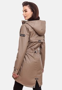 Waterproof beige raincoat with a hood, drawstring waist, and snap button accents. Features a back vent and logo patches on sleeves.