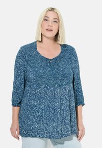 Blusa a stampa floreale blu con maniche 3/4, scollo rotondo e dettaglio di vita arricciata. Tessuto leggero con una texture morbida.