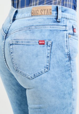 Heledad sinised teksad, millel on kulunud tekstuur, punase logo sildiga tagakotil ja nahkne vöölabel.