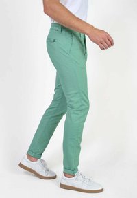 Mintgroene slim-fit chinos met een gladde textuur, zijzakken en een knoopsluiting, gecombineerd met witte lage sneakers.
