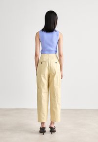 Haut sans manches à rayures de couleur lilas clair associé à un pantalon cargo jaune taille haute avec des poches latérales et des accents de boutons noirs.