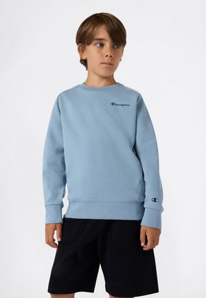 Sweat-shirt bleu clair avec de longues manches, poignets côtelés et un logo "Champion" noir brodé sur la poitrine, associé à un short noir.