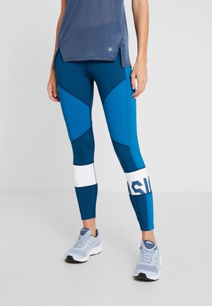 Jambes portant des leggings de sport bleu et turquoise à motifs avec des bandes blanches près des mollets, associés à des chaussures de course bleu clair et un haut bleu.