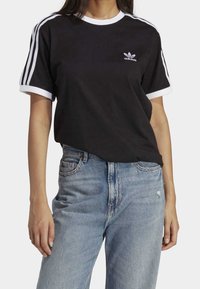 Černé bavlněné tričko s bílým límečkem a manžetami, s třemi bílými pruhy na rukávech a malým logem Adidas na hrudi.