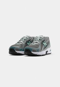 Une paire de chaussures de course en mesh grises et teal avec des lacets blancs et des semelles blanches épaisses, positionnées côte à côte sur un fond blanc.